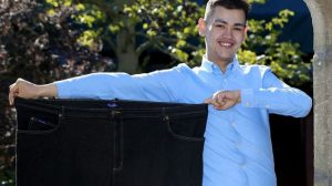 The 24-year-old, pictured with a pair of his old trousers, lost a massive 30 inches from his waistline
